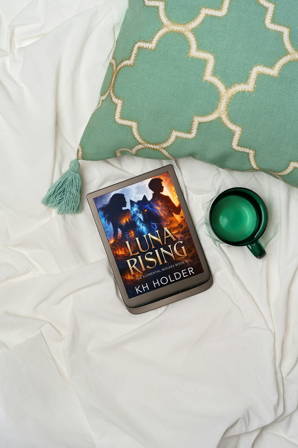 E-reader with 'Luna Rising' book on a white surface with a green mug and decorative pillow.